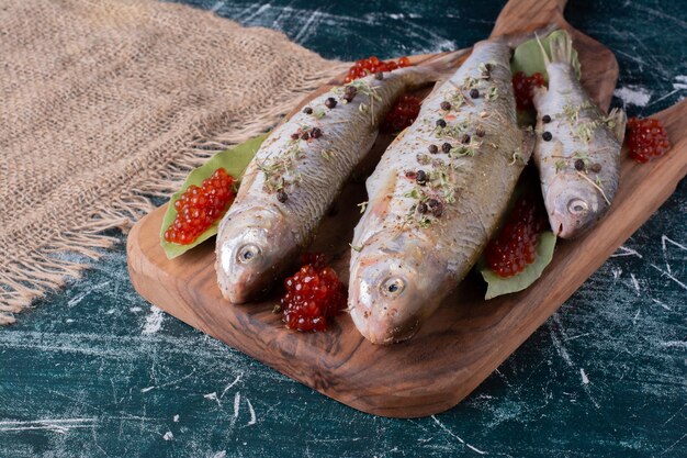 Raw whole fishes with red caviar on wooden board. 