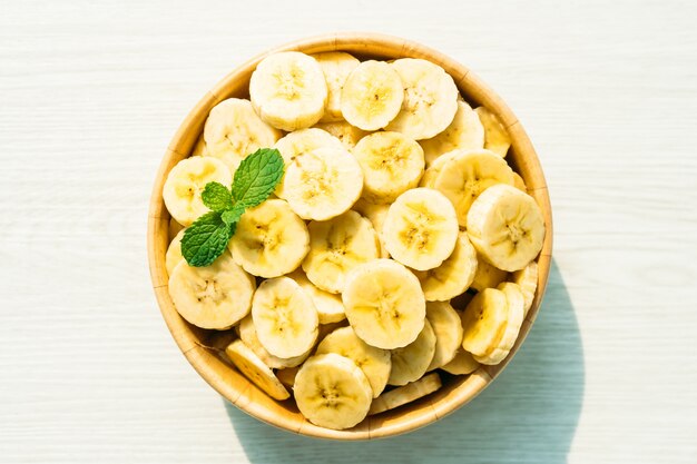 Raw yellow banana slices in wooden bowl