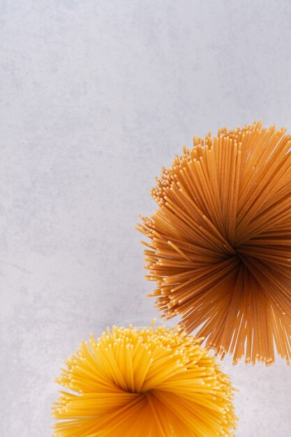 Raw yellow and brown spaghetti on white surface