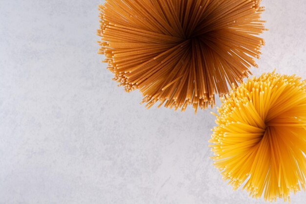 Raw yellow and brown spaghetti on white table.