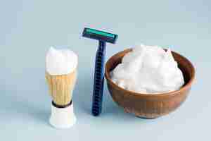 Free photo razor; shaving brush and bowl of foam against blue backdrop