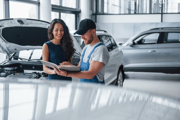 Read this carefully. Woman in the auto salon with employee in blue uniform taking her repaired car back