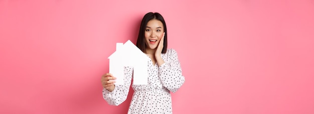 Взрослая азиатская женщина, занимающаяся недвижимостью, ищет дом, холдинг модель дома и улыбается промо брокера.