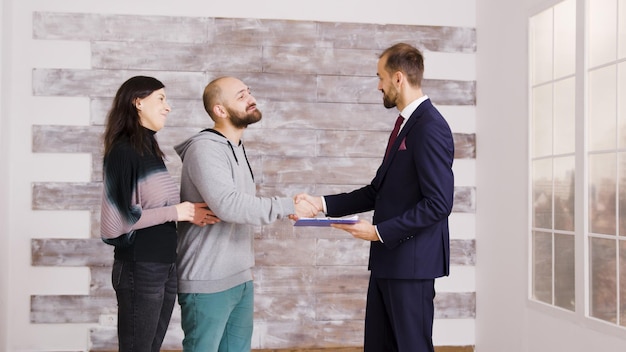 Foto gratuita agente immobiliare in giacca e cravatta che dà le chiavi alla giovane coppia dopo aver firmato il documento. coppia che diventa proprietaria di casa.