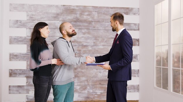 Real estate agent in business suit giving keys to young couple after signing document. Couple becoming homeowners.