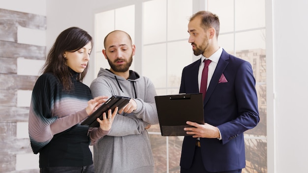 Free photo real estate agent talking with couple and holding documents homeowning contract in new apartment.