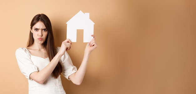 Real estate angry girl showing house cutout and frowning upset complaining on apartment standing aga