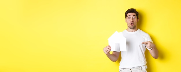 Foto gratuita il concetto di bene immobile ha eccitato l'uomo che punta il dito contro il modello di casa di carta alla ricerca di un ove piatto in piedi