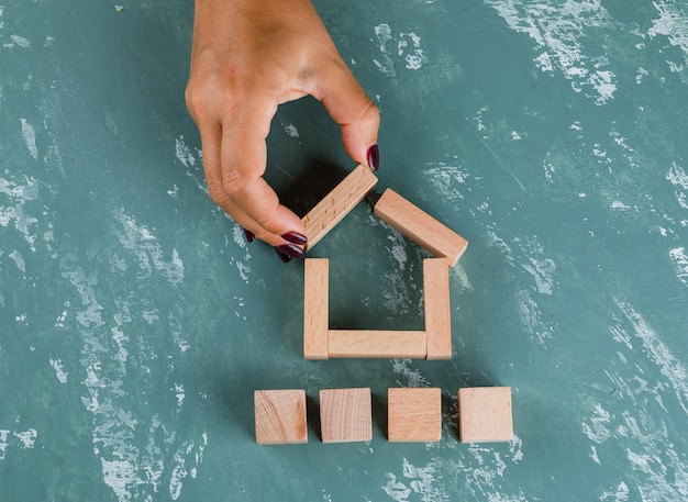 Real estate concept with wooden blocks flat lay. woman making house model.