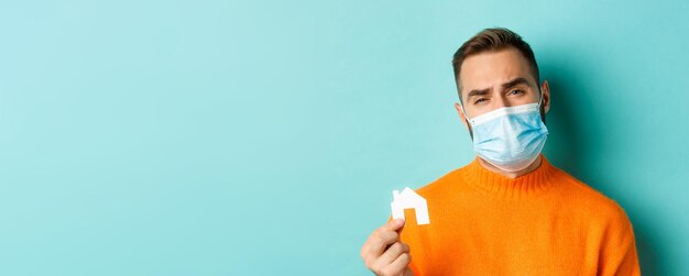 Real estate and coronavirus pandemic concept closeup of sad man in face mask showing face mask and g