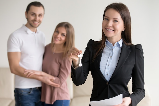 Real estate deal. Female smiling realtor showing keys to flat