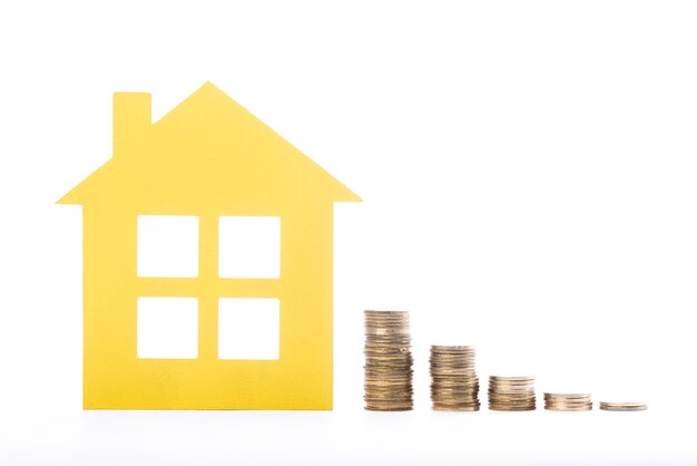 Real estate house and piles of coins on white background