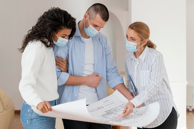 Realtor and couple with medical masks looking at house plans