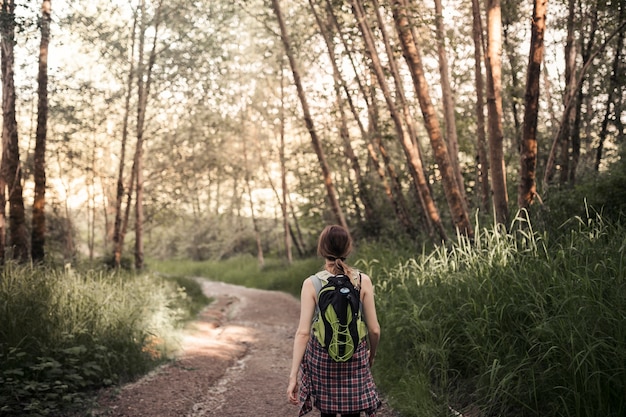 Rear vie of woman walking on the dirt road in the forest