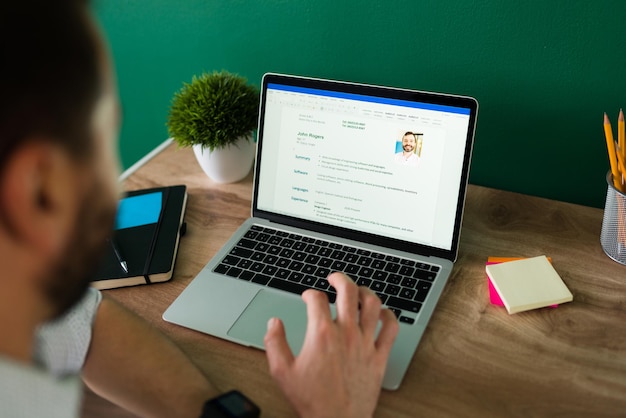 Rear view of an adult man searching for a new job and working on writing his resume on the laptop