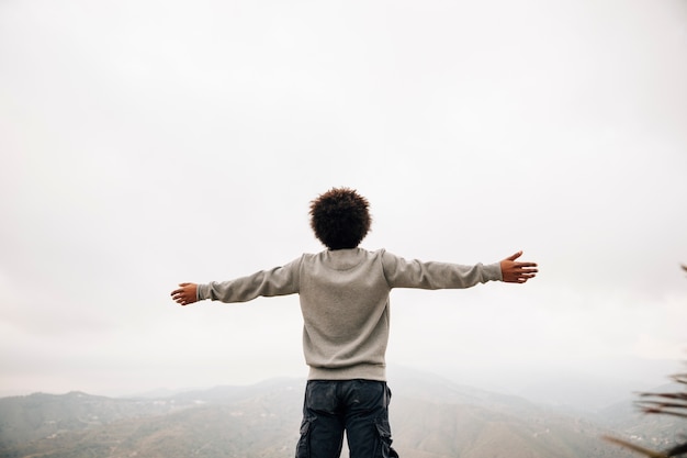 Вид сзади африканского молодого человека, стоящего на вершине горы, протягивающей его руку
