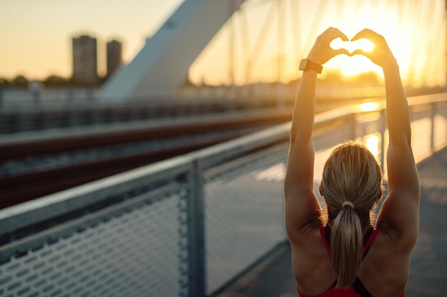 Rear view of athletic woman showing heart shape at sunset