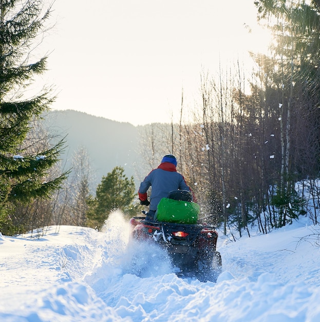 산에서 겨울에 사륜차 ATV를 운전하는 자전거 타는 사람의 후면보기