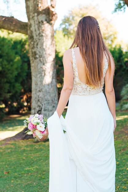 手に花束を持って公園に立っている花嫁の背面図