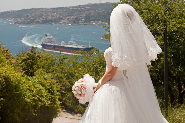 Вид сзади невесты с букетом, глядя на залив