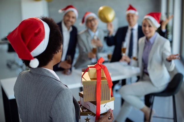 Retrovisione della donna di affari che sorprende i suoi colleghi con i regali di natale sulla festa dell'ufficio