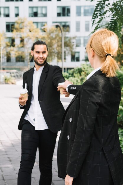 Rear view of a businesswoman taking takeaway coffee cup from smiling man's hand