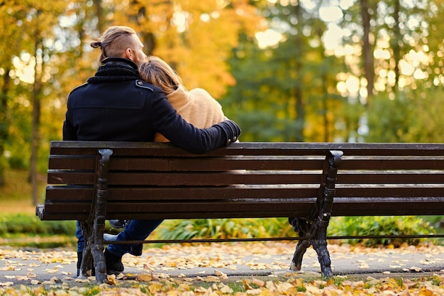 Rear view of couple sits on a bench in an autumn park.