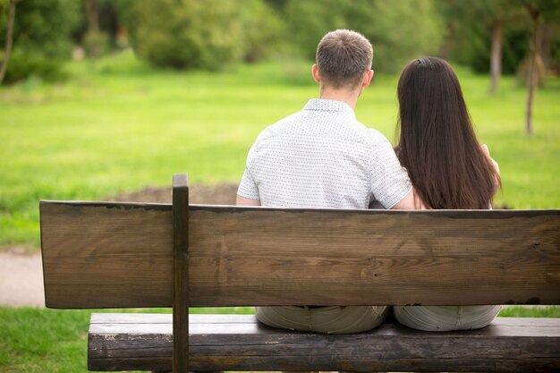 Rear view of couple sitting on a wooden bench outdoors