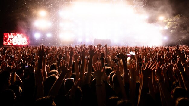 Rear view of excited people with arms raised having fun while watching confetti fireworks in front of the stage at music festival Copy space