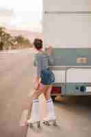 Free photo rear view of a female skater standing near the caravan peeking on road