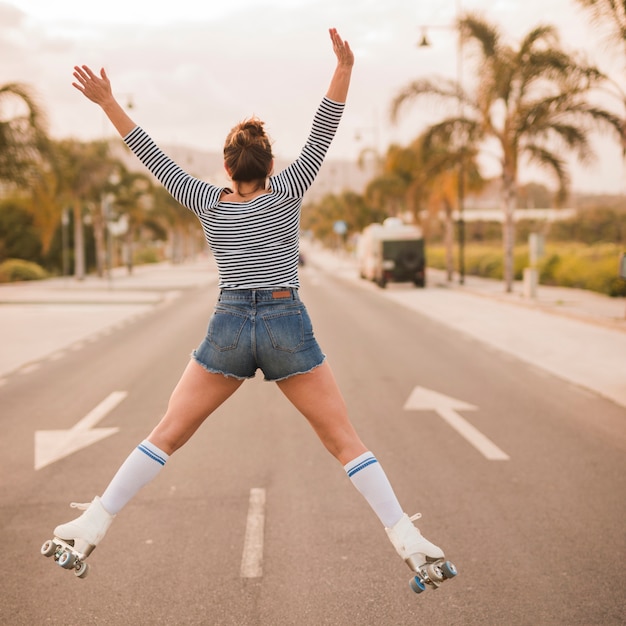 떨어져 그녀의 다리와 팔을 가진 여성 스케이팅의 후면보기 제기 도로에 점프