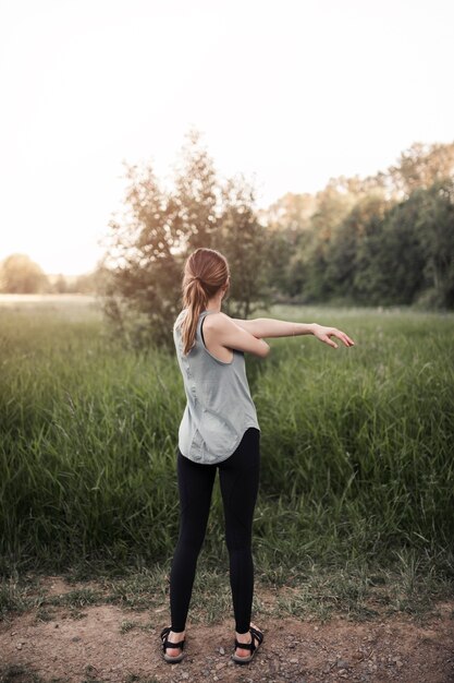 Rear view of fitness young woman stretching her hand standing in field