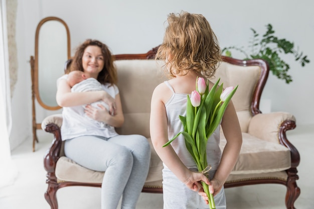 Rear view of girl holding tulip flowers behind the back for her mother