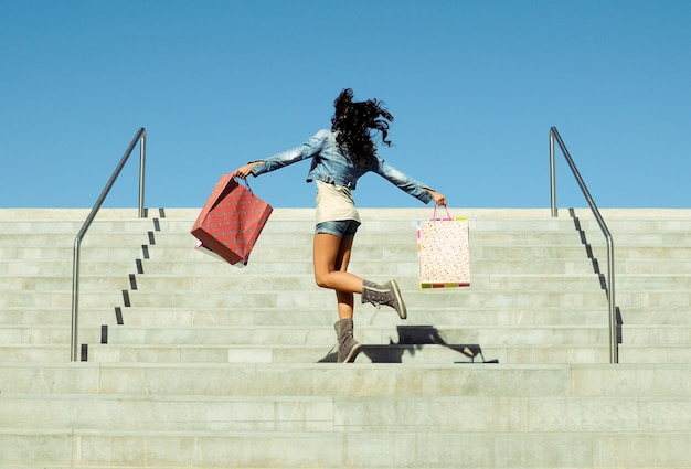 Rear view of girl jumping with shopping bags on the stairs