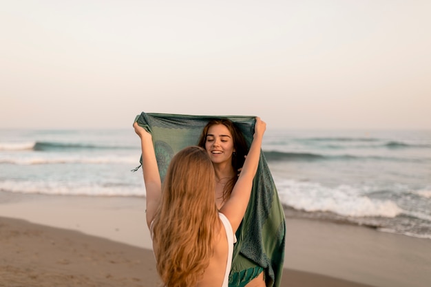 Vista posteriore della ragazza ponendo la sciarpa sulla testa del suo amico in spiaggia