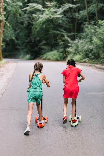 Rear view of girl riding push scooters on road