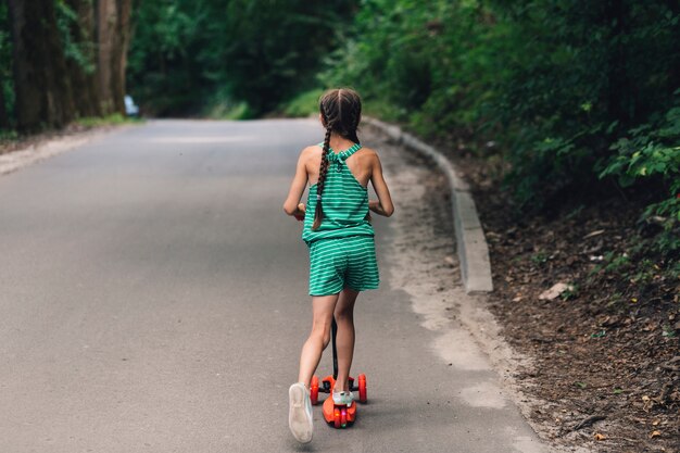 Rear view of a girl riding scooter on straight road