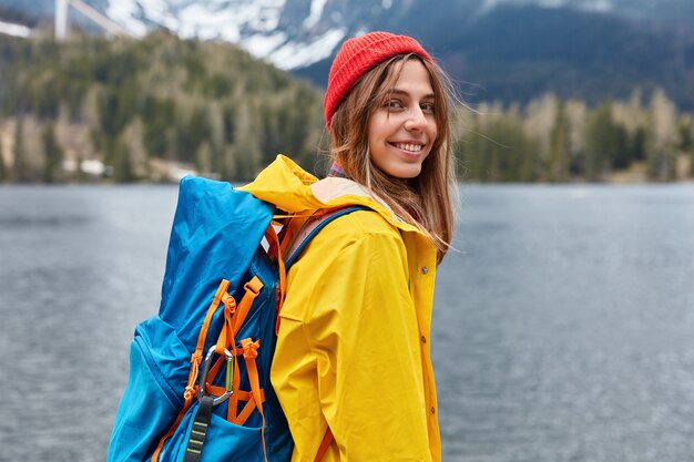 Rear view of happy young European woman enjoys nice serene day, nature landscape scenery, carries rucksack