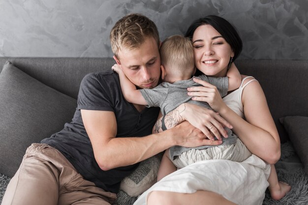 Rear view of a little boy hugging her parents sitting on sofa