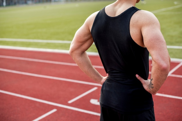 Retrovisione di un atleta maschio con le mani sull'anca che sta sulla pista di corsa