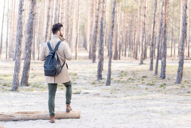 Вид сзади мужской турист с его рюкзаком, стоя в лесу