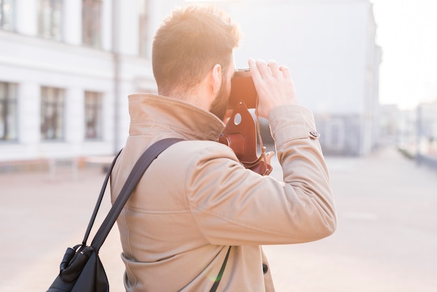 Вид сзади мужской путешественник, фотографировать в городе с камерой