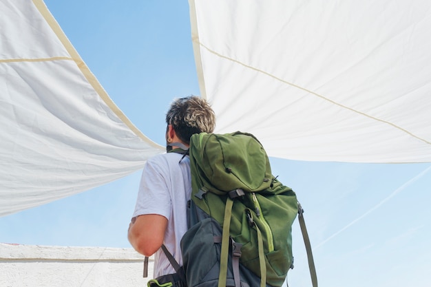 Rear view of man carrying green backpack standing under sunshade