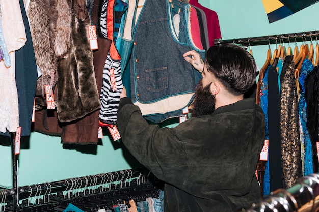 Rear view of a man choosing clothes hanging on the rail in the clothing shop