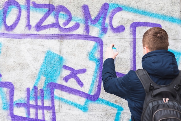 Rear view of a man drawing graffiti on wall