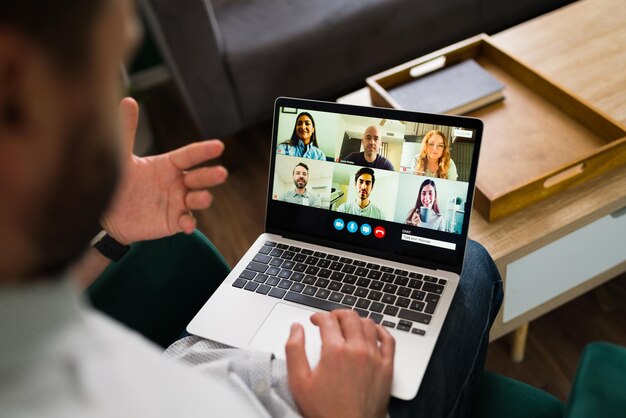 オンラインで仕事の会議をしている男性の背面図。彼のラップトップでのビデオ通話中に同僚と話している成人男性