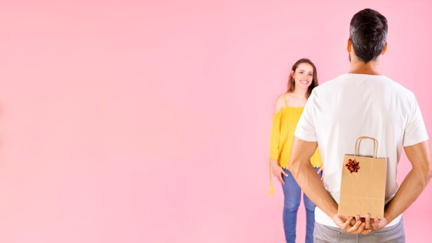 Rear view of man hiding gift from her girlfriend over pink background