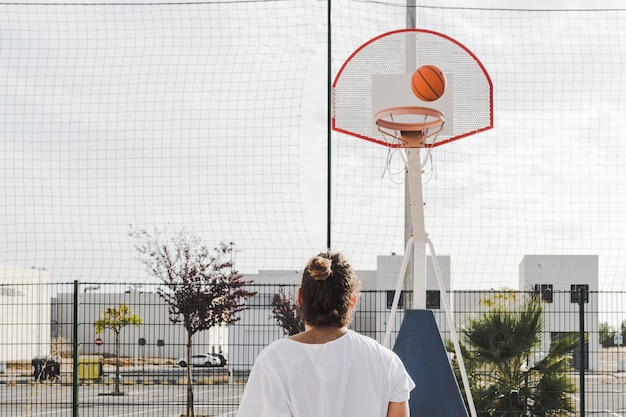 Rear view of a Man looking at basketball going through hoop in court