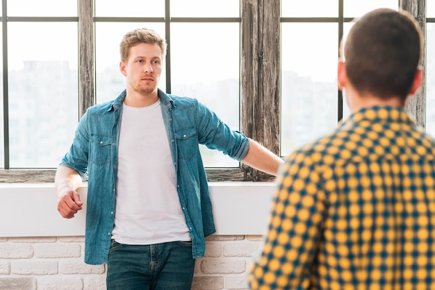 Foto gratuita vista posteriore di un uomo che guarda il suo amico appoggiato vicino alla finestra