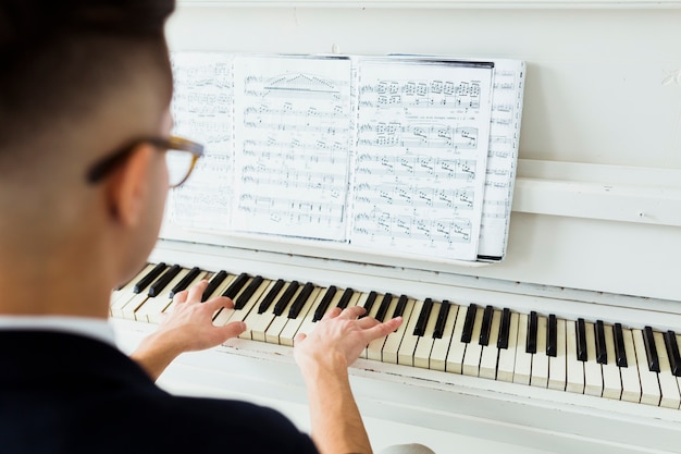 Вид сзади человека, смотрящего на музыкальный лист, играющий на пианино